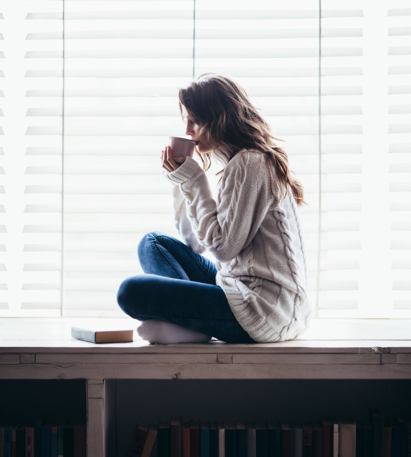 Mujer sentada junto a una ventana con una taza entre las manos, en un momento de calma